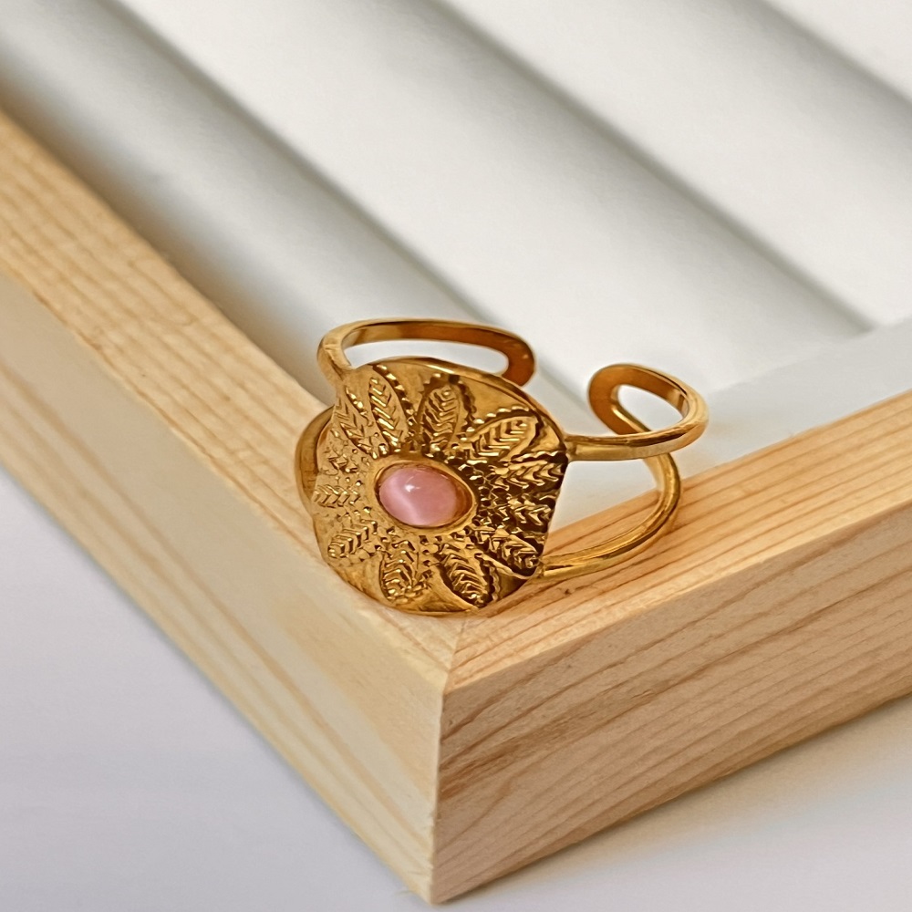 Δαχτυλίδι χρυσό με σχηματισμένα ανάγλυφα φύλλα και ροζ πέτρα στο κέντρο.